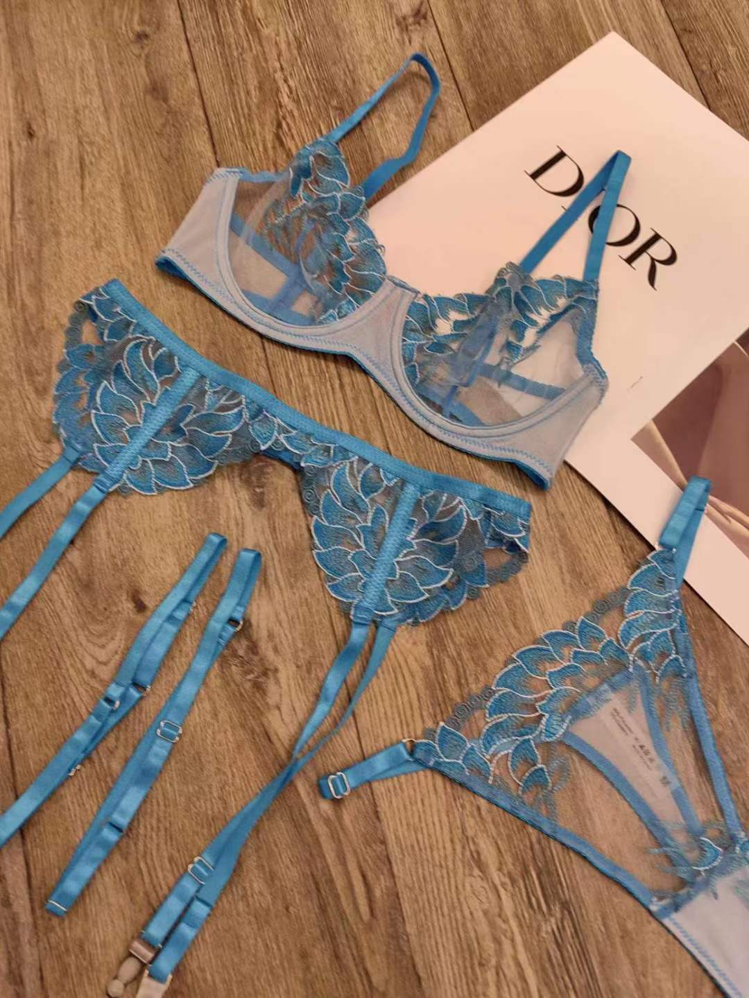 Blue anti-sagging lace embroidery three-piece lingerie set with delicate floral designs on wood background.