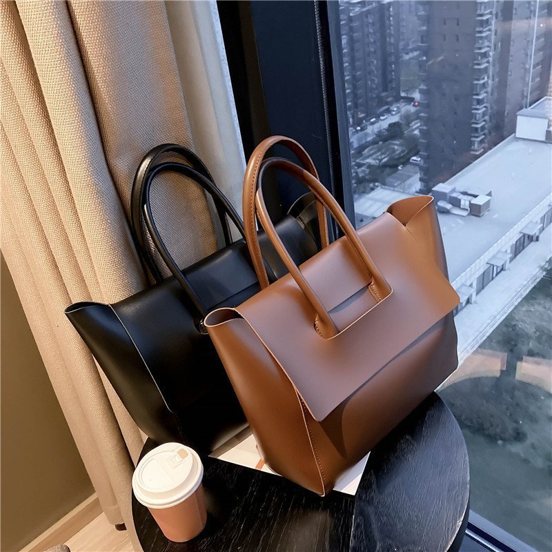 Shoulder bags with large capacity in brown and black on a table near a window.