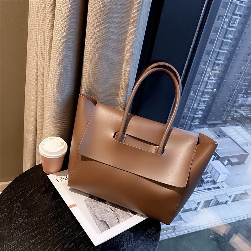 Large capacity brown shoulder bag with stylish design, displayed next to a coffee cup by a window.